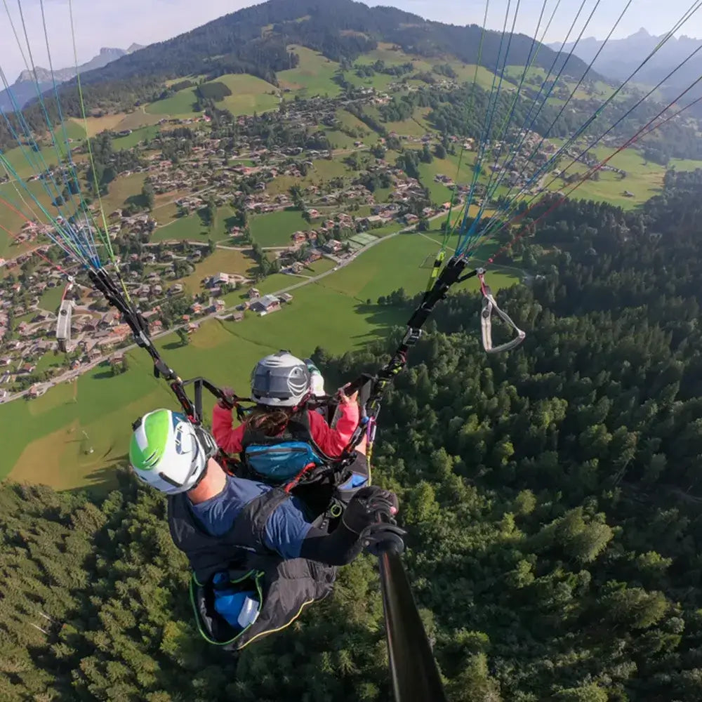 Paragliding adventure over lush green fields and villages, capturing the thrill of a tandem flight in the Aravis region.