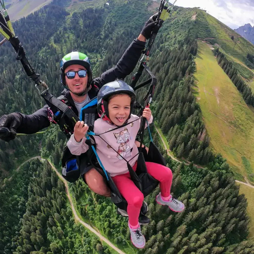 Enfant et moniteur en vol de parapente au-dessus des montagnes, offrant une expérience aérienne inoubliable.